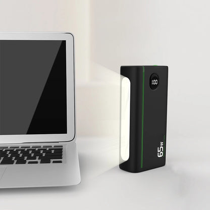 65W Two-Way Fast Charging 26800mAh Power Bank, standing upright with the flashlight turned on, showcasing additional features next to a laptop