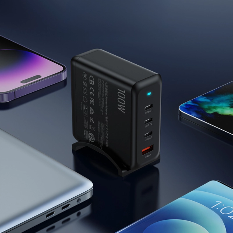 PD100W GaN Multi-Port Charger for Laptops & Phones, black variant in an angled view on a reflective surface, surrounded by an iPhone, Android phone, and laptop